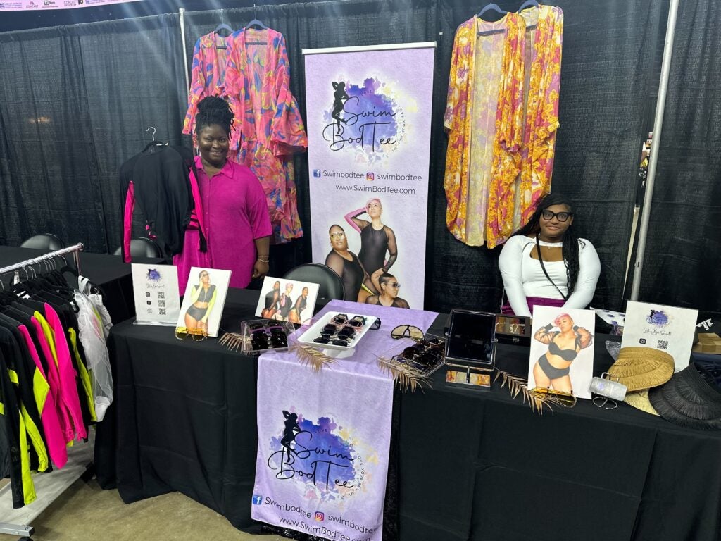 Women with SwimBodtee, a plus-sized swimsuit store, pose in front of their stall at the Wells Fargo Center